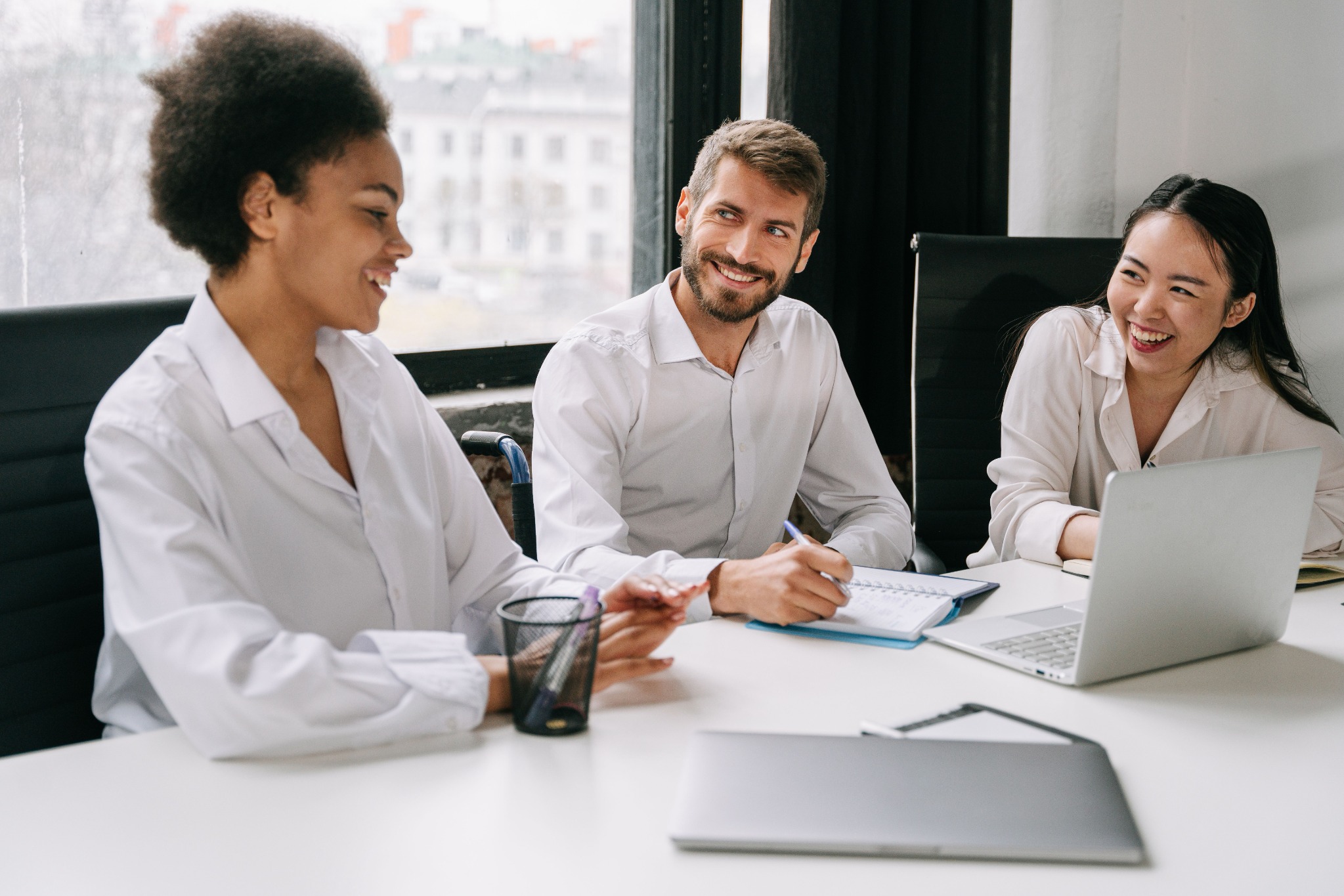 Three people discussing documents beside a laptop in a bright office